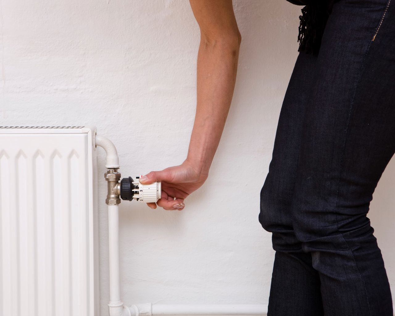 En hånd drejer på en termostat på en radiator