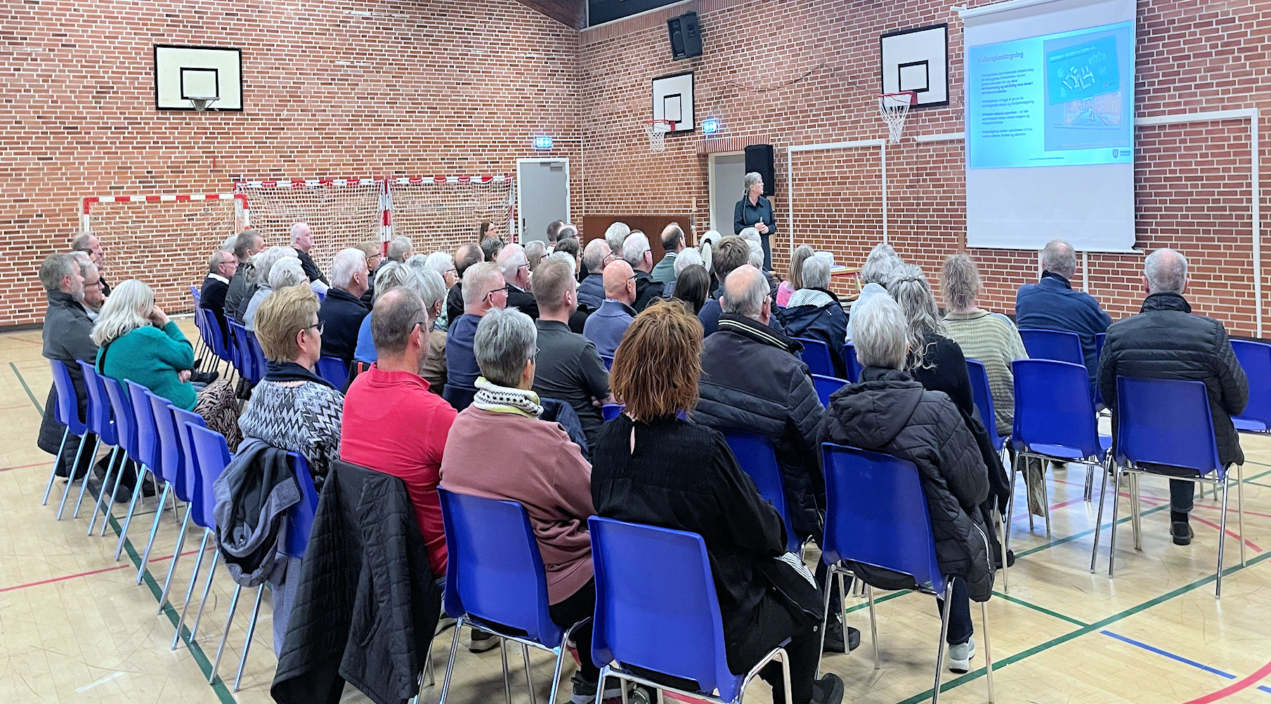 Voksne personer sidder i et lokale og lytter til oplægsholder