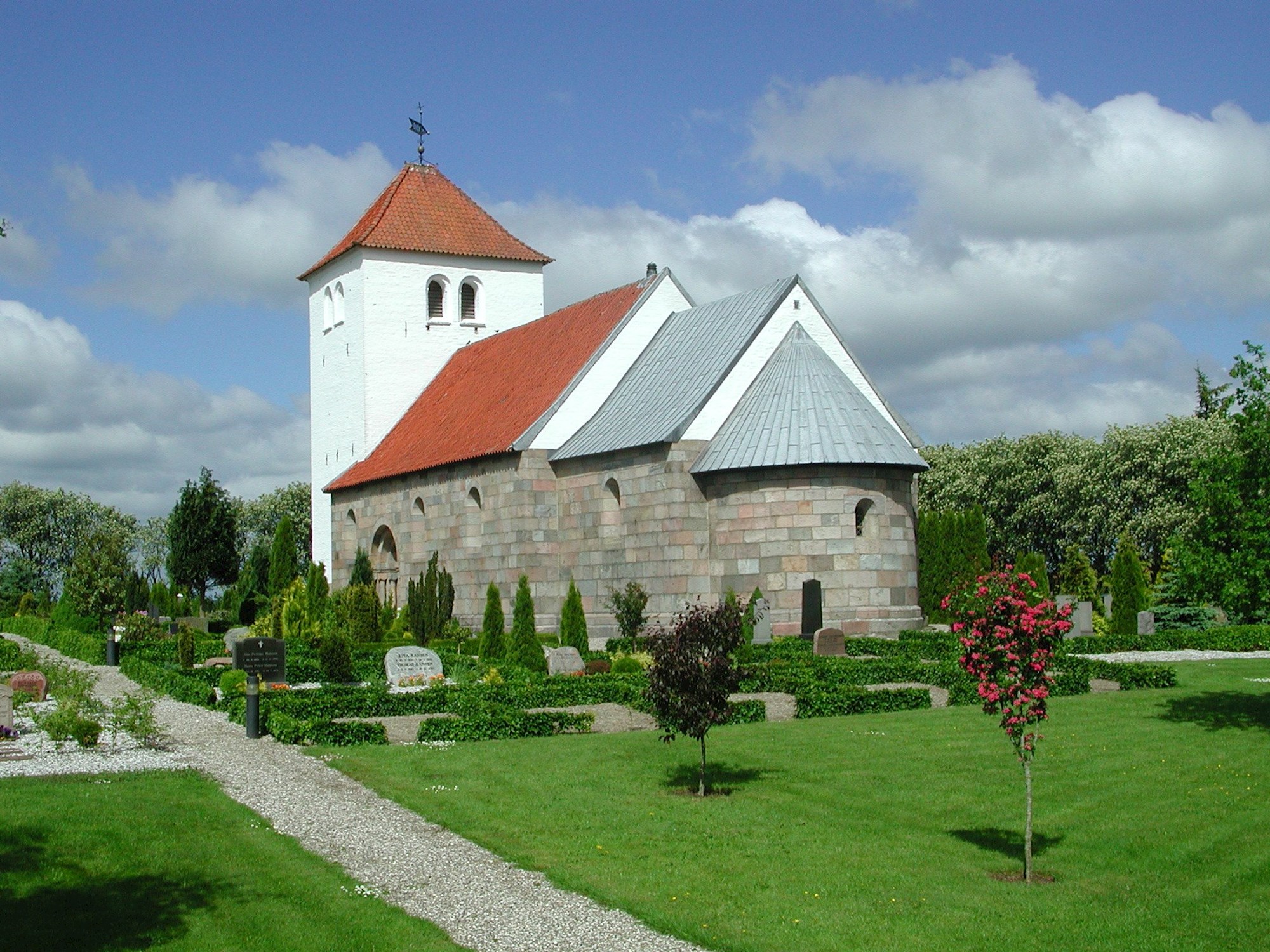 Kirke med rødt tag og grønt græs på kirkegården