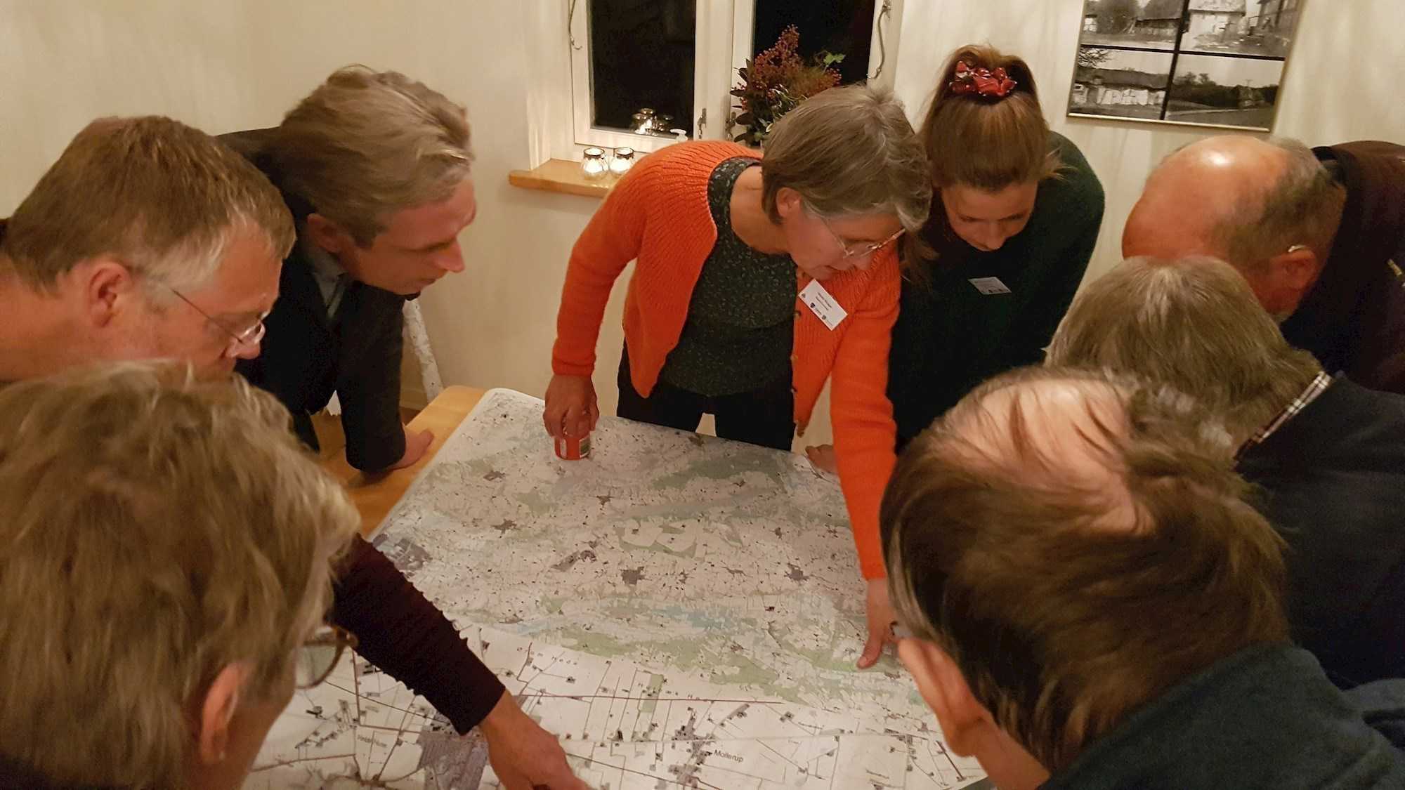 8 voksne samlet om et bord, hvorpå der ligger et kort