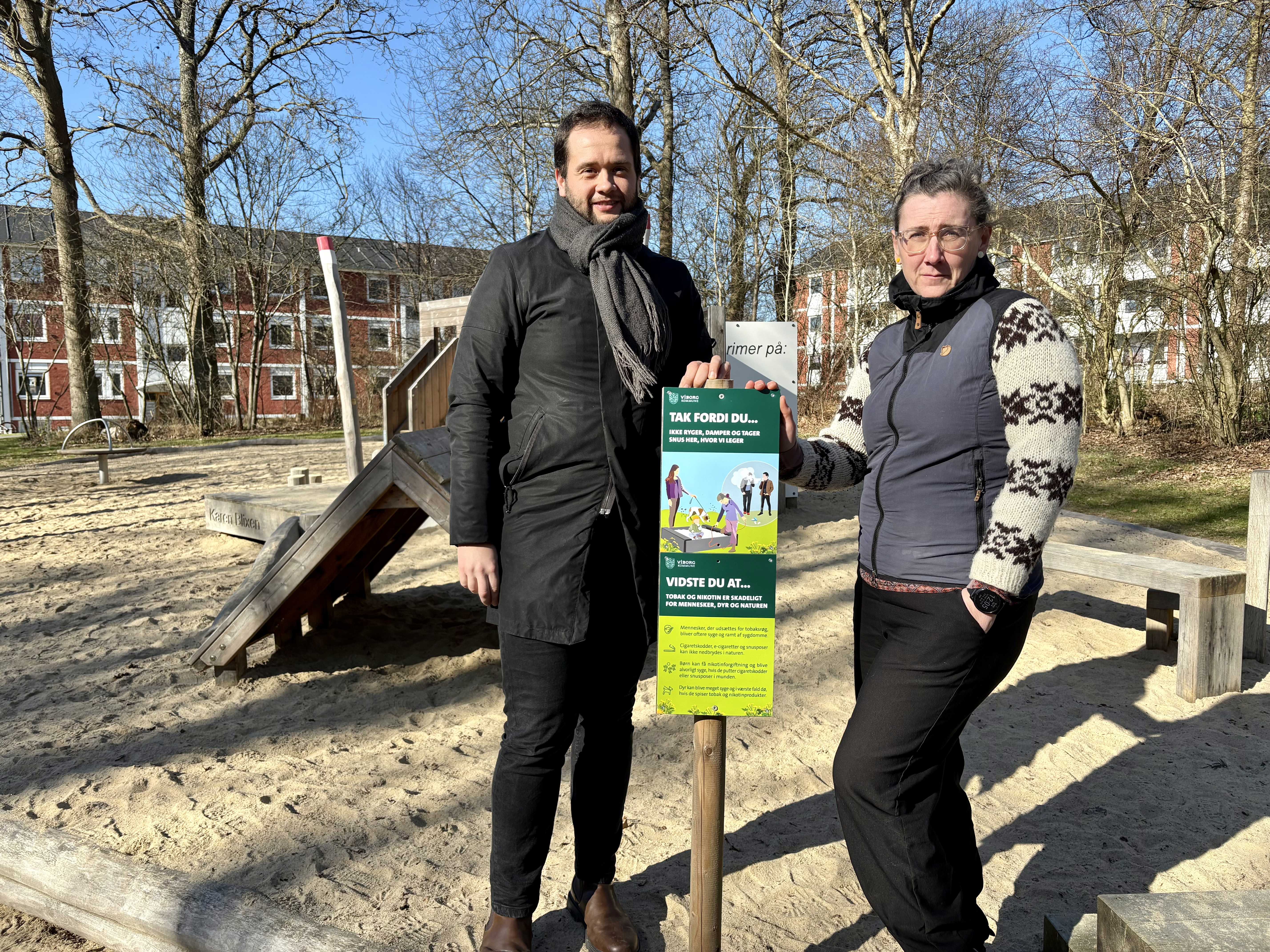 Dennis Krogsdal Laursen fra Sundhedscenter Viborg og Karen Hingkjær Carol Glerup-Nielsen fra Teknik & Miljø står bag et skilt ved en legeplads.